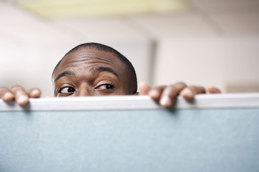 Man peeking over the top of a cubicle wall