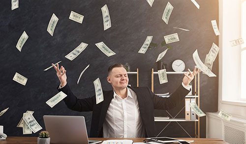 Man at desk with hands raised to enjoy the fact that money is falling down from above