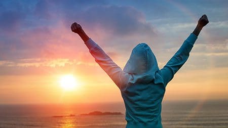 Person hands raised in triumph enjoys sunset