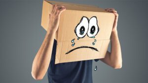 Man with cardboard box on his head. Box has crying face drawn on it.