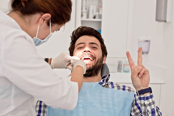 Man in dentist chair during exam flashes a peace sign