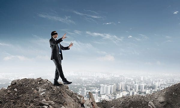 Man wearing blindfold is about to walk off edge of rubble pile