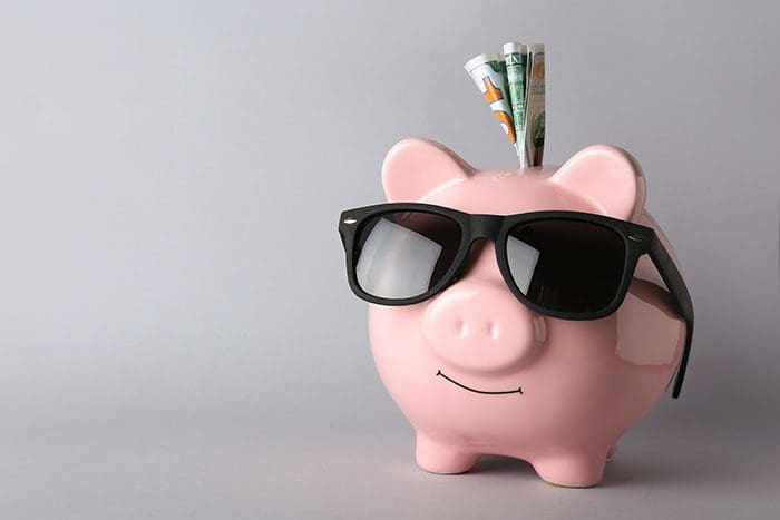 Piggy bank with sunglasses and smile, some cash sticking out of the top