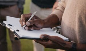 Cropped view of man writing something on paper on a clipboard