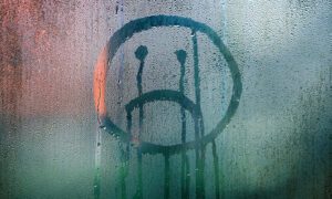Sad face that appears to be crying drawn on a steamed up window