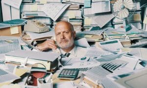 Businessman on phone in office buried in paperwork.