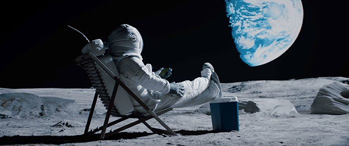 Astronaut in lounge chair sitting on moon looking at Earth in the sky