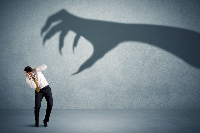 A shadow of a large claw reaches out to a cowering businessman