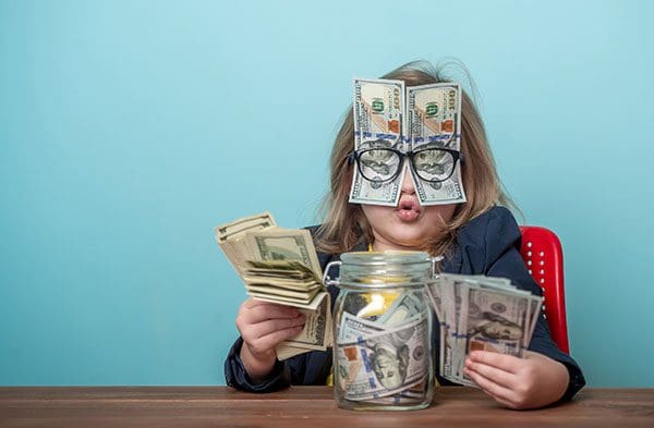 Child with money jar, money in her hands and also money held in place over her face with her eyeglasses